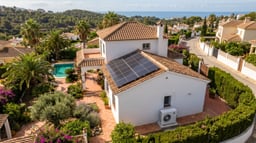 Vivienda unifamiliar española con placas solares en cubierta y bomba de calor aerotérmica en lateral.